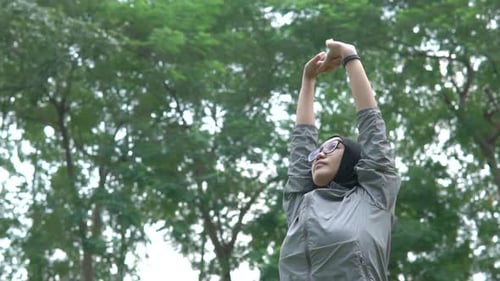 Southeast Asian hijabi woman stretching outdoors in park