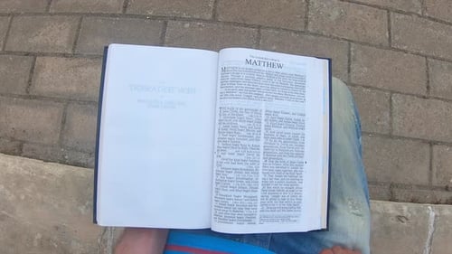 Mann mit der neutestamentlichen Bibel auf dem Schoß, liest und blättert die Seiten aus seiner Sicht um.