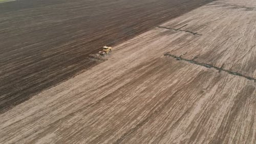 Large Yellow Tractor Cultivates Field After Harvesting Grain Crops