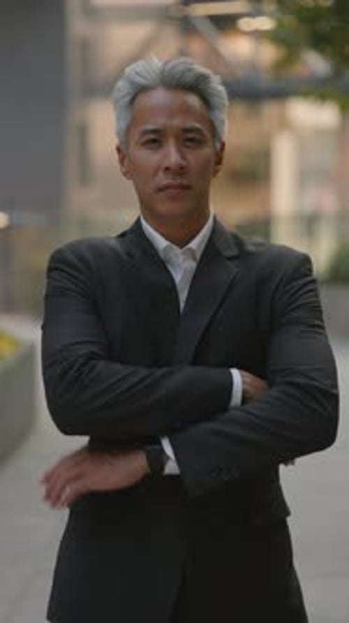 Portrait of Mature Asian Top Manager Crosses Arms Near Corporate Building