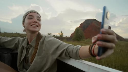 Fröhliche Tramperin macht Selfies auf dem Smartphone, während sie im Kofferraum fährt