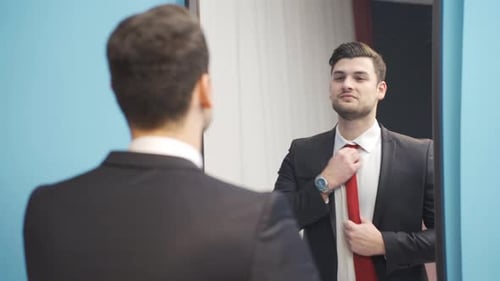 Young Man in Suit Adjusting Tie in Mirror