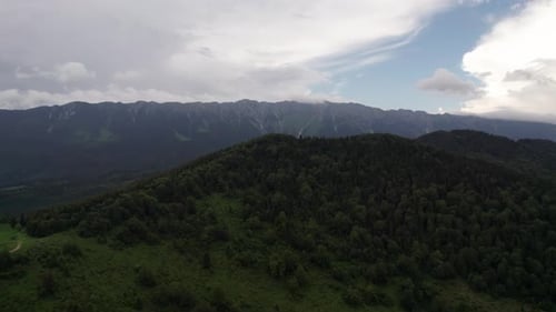 Lush green mountain landscape under a cloudy sky, aerial view