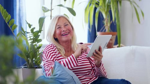 Smiling senior woman using tablet on sofa at home