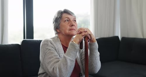Contemplative Senior Woman Sitting with Cane Indoors