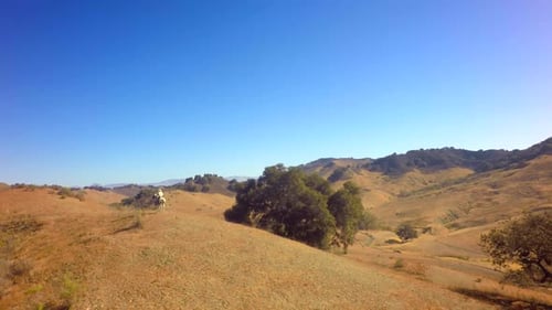Cowboy On Horseback Traveling On Mountain Range On Sunny Day