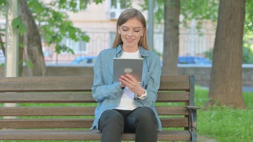 Woman Using Tablet while Sitting on Bench in Park