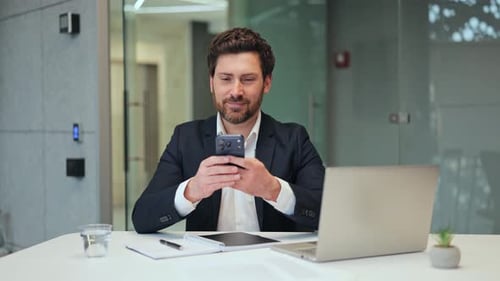 Professional Man Smiles Using Smartphone in Modern Office
