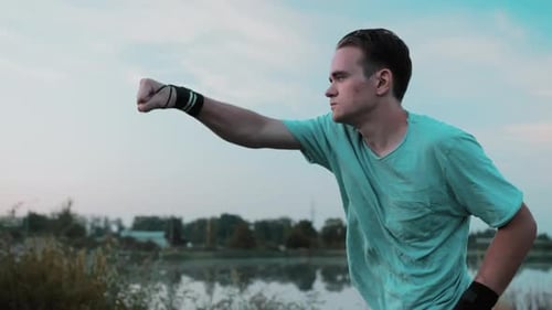 A Young Guy Is Boxing Training In Nature Behind A Lake Or A Quarry