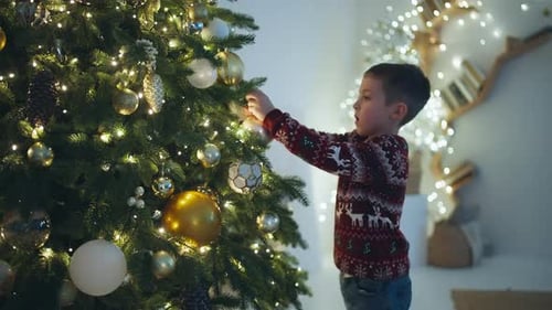 Boy Decorates Christmas Tree with Colorful Baubles