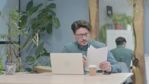 Man Works at Laptop with Documents in Office