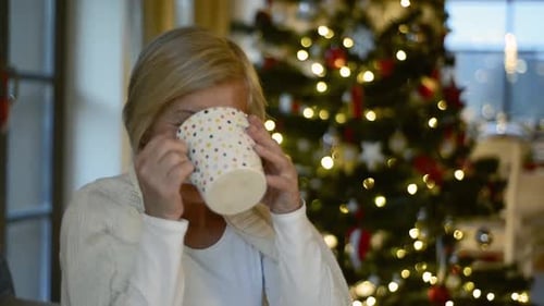 Woman with Hot Drink Near Christmas Tree Smiling