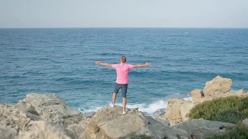 A man standing on the rocky coast, enjoying the view of the sea