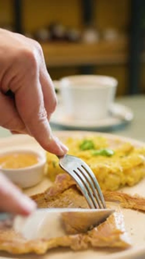 Cutting Chicken Breast on Plate with Scrambled Eggs