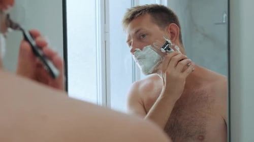 Caucasian Handsome Yong Man with Shaving Foam on His Face While Shaving His Beard Standing in the