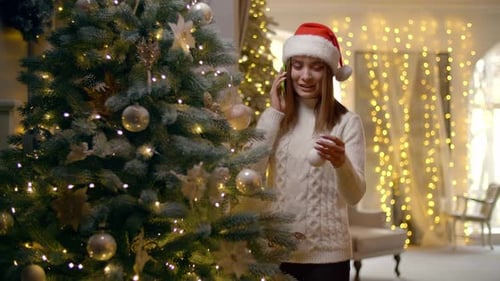 Jovem mulher conversa por telefone enquanto decora a árvore de Natal