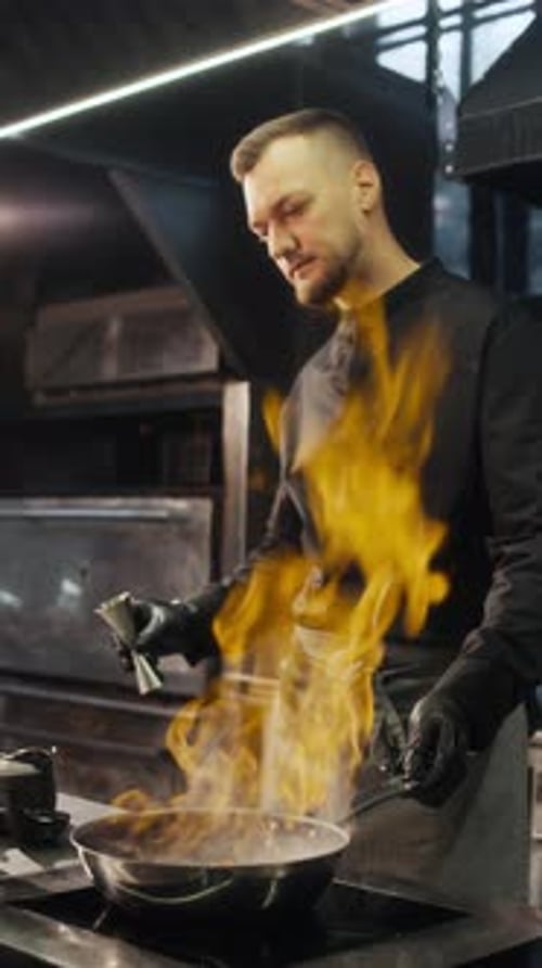 Koch kocht mit flammender Pfanne in der Küche