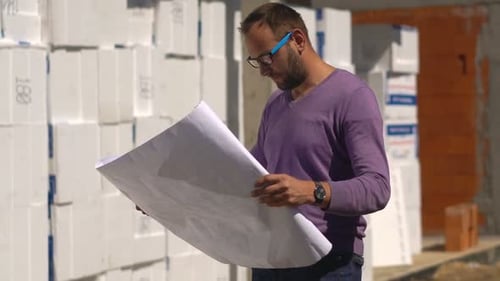 Young Man Reading Blueprints and Checking New House 30s