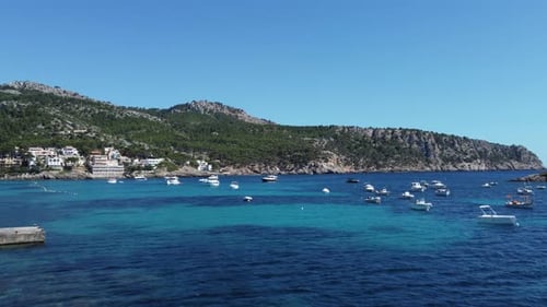 Drone flying over crystal clear blue waters in a quiet natural harbour with boots and yachts coming