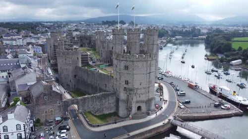 Ancient Caernarfon castle Welsh harbour town aerial view medieval waterfront landmark fast orbit lef