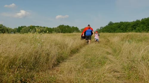 Carefree Family in Superhero Costumes Running on Green Field at Countryside