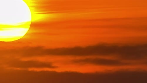 View of yellow sun setting in the orange sky with dark clouds passing by in timelapse. Close up view