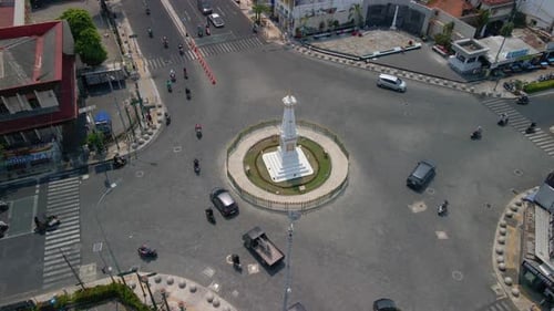 Aerial orbiting shot of Tugu Yogyakarta with busy traffic on road in city during sunny day