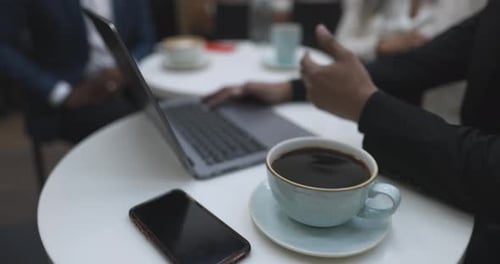 Business people enjoying coffee and teamwork at laptop in bright cafe
