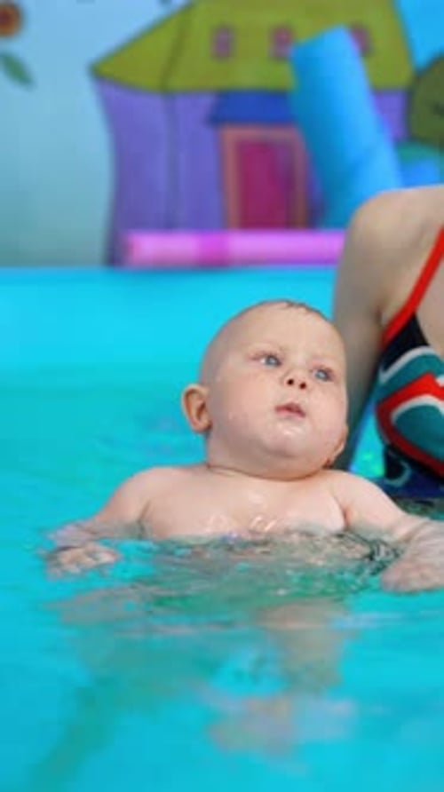Teaching a little toddler baby to swim in the pool.