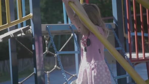 Shot in slow motion of a 4 years old girl climbing a structure in a playground during a sunny day.