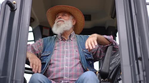 Old Positive Farmer Sitting in Tractor Looking Around in Slow Motion Front View Portrait of