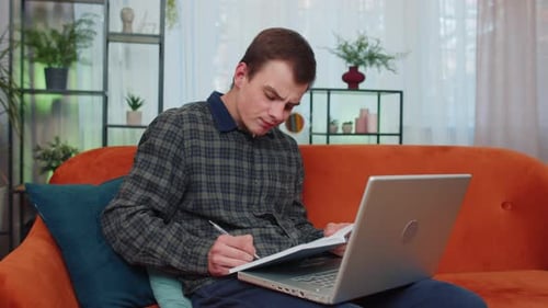 Young Adult Studying at Home With Laptop and Notebook
