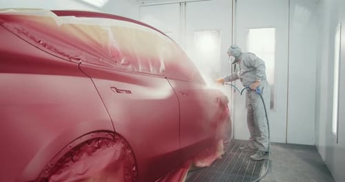 Man Sprays Red Car with Paint in Auto Shop