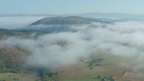 Aerial flyover shot high above the clouds looking out on a pastoral landscape.