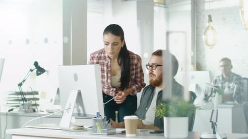 In a Busy Office Beautiful Girl Approaches Her Male Colleague Who is Sitting at His Desk and Points