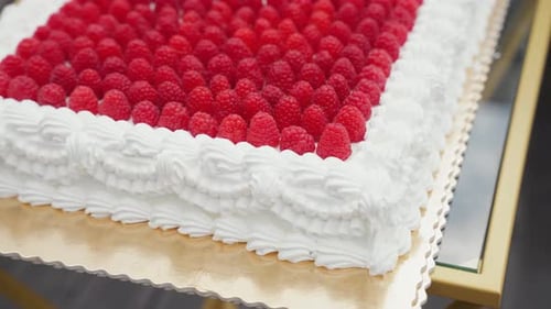 Close-up of a rectangular raspberry cake topped with fresh red berries and decorated with intricate
