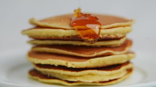 Closeup Amber Yellow Sweet Honey Falling on Pile of Pancakes Flowing Down Closeup Delicious