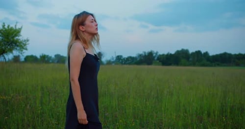 Beautiful female blonde model in black long dress walking on a meadow