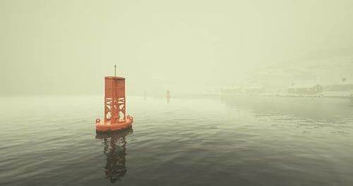 La boya flota en aguas brumosas cerca de una ciudad costera mientras la niebla envuelve el paisaje
