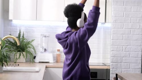 Woman Dancing Energetically with Headphones in Kitchen