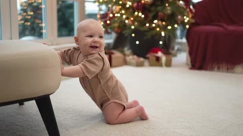 Happy baby learning to stand near Christmas tree