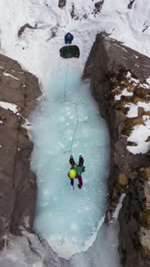 Frau führt auf Eiseis und klettert auf einem gefrorenen Wasserfall Vertikales Video aus der Luft