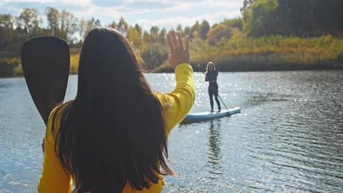 Woman Waving to Paddle Boarder on Lake