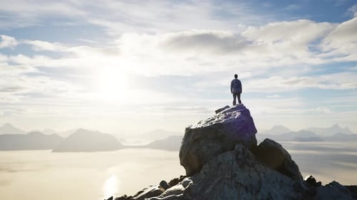 Adventurous Male Hiker Standing on Dramatic Rocky Peak. Low Clouds and Mountain Landscape. Sunny Day