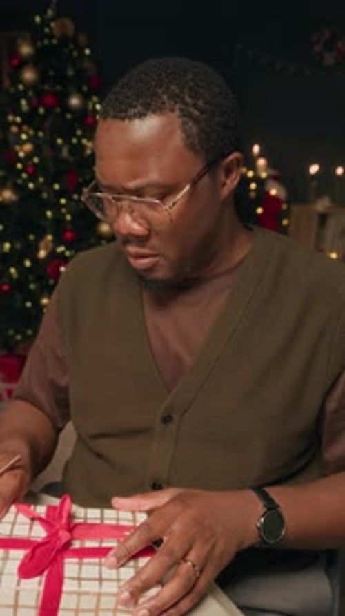 Man Unwraps Christmas Gift near Decorated Christmas Tree