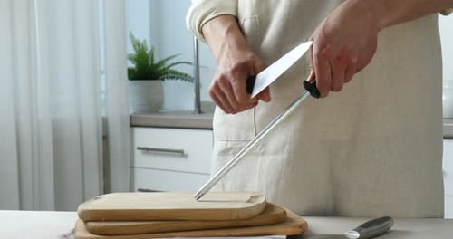 Man sharpening knife with sharpener at beige table indoors, closeup