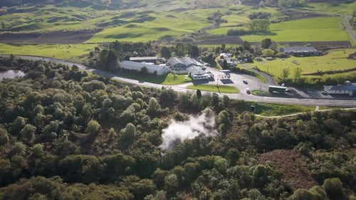 Aerial high angle orbit around a steaming natural hot spring within dense bushland and a country roa