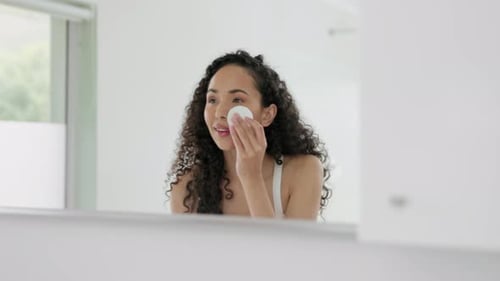 Woman Cleans Face with Cotton Pad in Bathroom