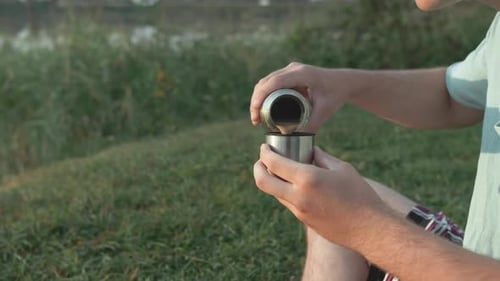 A Young Guy Drinks Coffee From A Thermos Behind A Lake