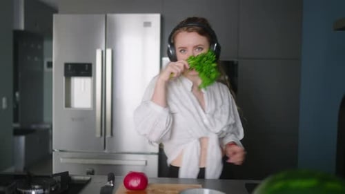 Woman in Headphones Making a Salad of Vegetables and Has Fun Dancing at Modern Kitchen Island Young